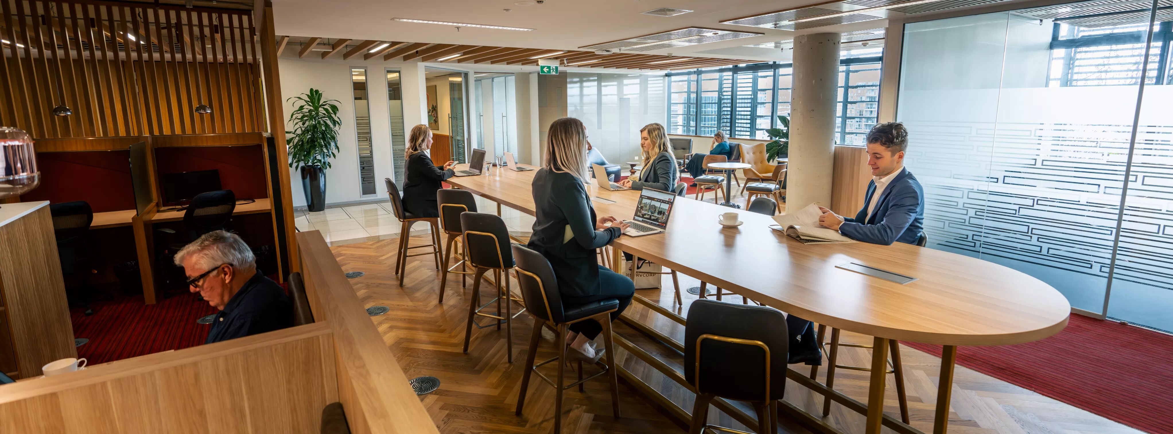 Clients working in a modern coworking space on a long table, in Servcorp Nishi Building, Canberra